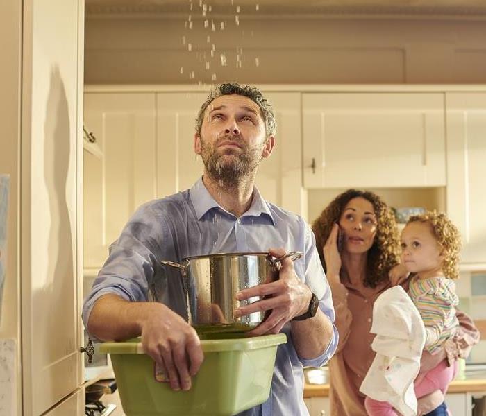 A man, woman, and child catching water in buckets in a kitchen. 